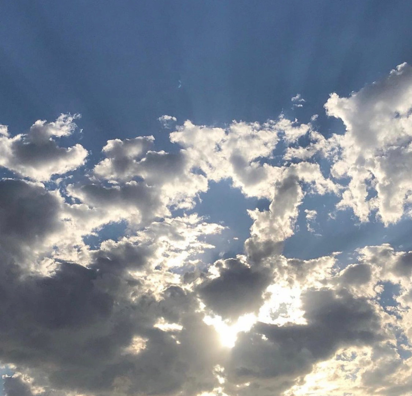 Sunlight breaks through white and gray clouds with bright edges against a blue sky.