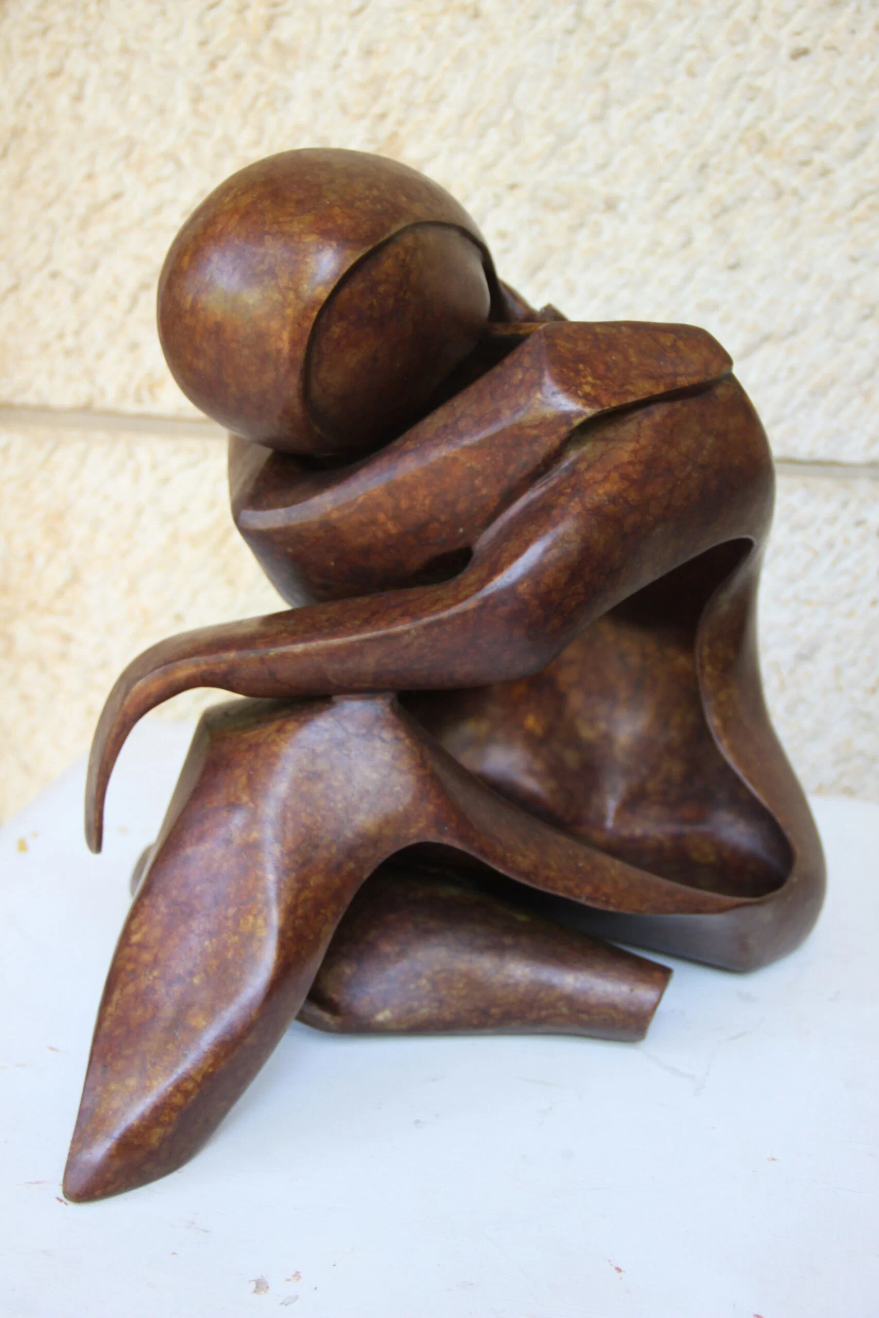 Daniela Ament: The Inner Life Given Form | ArtTour International A bronze figure with a lowered rounded head and curved limbs folded inward, with a warm brown patina and open spaces between the forms.