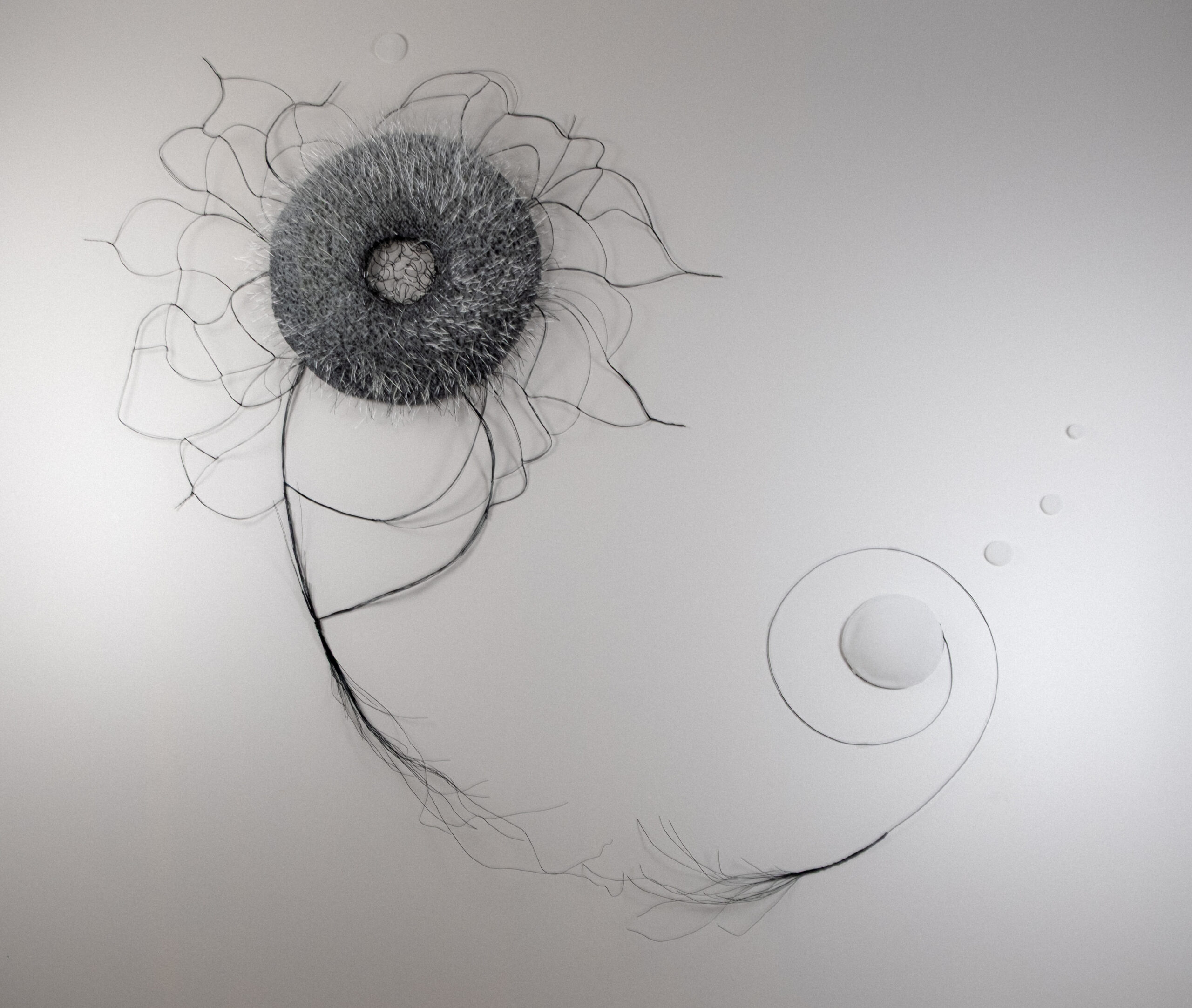 Irina Howard: Giving Shape to the Unseen | ArtTour International A circular textured sculptural form with fine radiating wires and a long looping curve across a pale background.