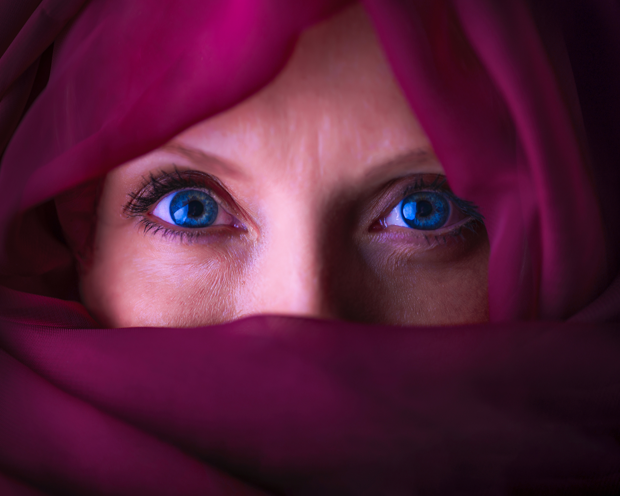 Gene Sellers: Photographs at the Edge of a Story | ArtTour International Close view of bright blue eyes surrounded by folds of deep magenta fabric.