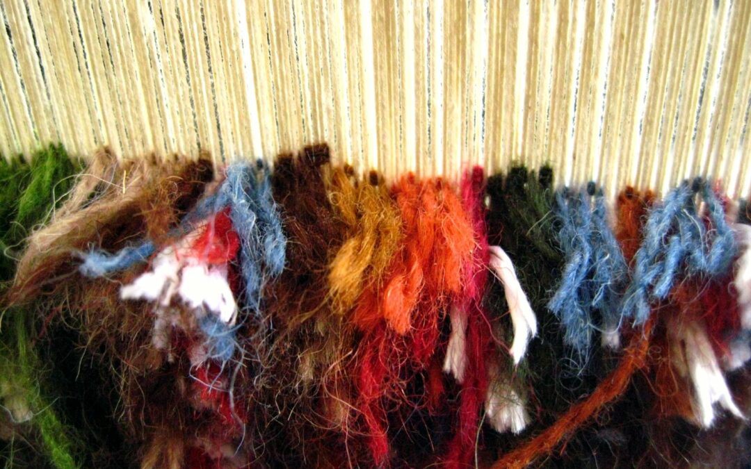 Hands working on a colorful textile at a vertical loom